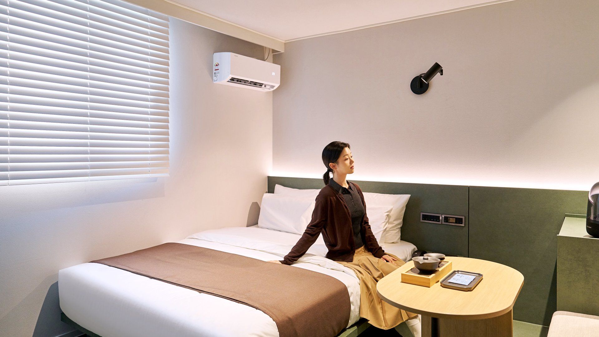 Habitación de hotel con cama, mesita de noche, aire acondicionado e iluminación en la pared.