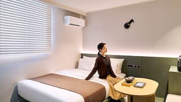 Habitación de hotel con cama, mesita de noche, aire acondicionado e iluminación en la pared.