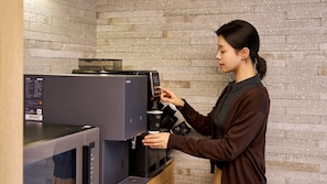 A person operating a coffee machine with a digital interface, in a room with a brick wall background.