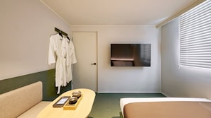 Habitació d'hotel amb llit, sofà, televisió penjada a la paret i una porta.