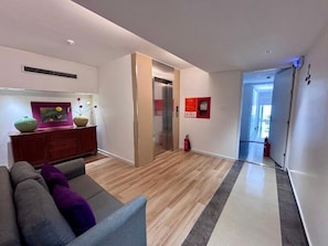 A modern living room with a sofa, a wooden floor, a fireplace, and a hallway leading to an elevator. - The Charm Boutique Hotel  (thanh pho hue)