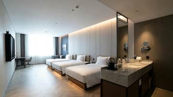 Habitación de hotel con dos camas, un escritorio, una silla, un espejo grande y un baño con lavabo y espejo.
