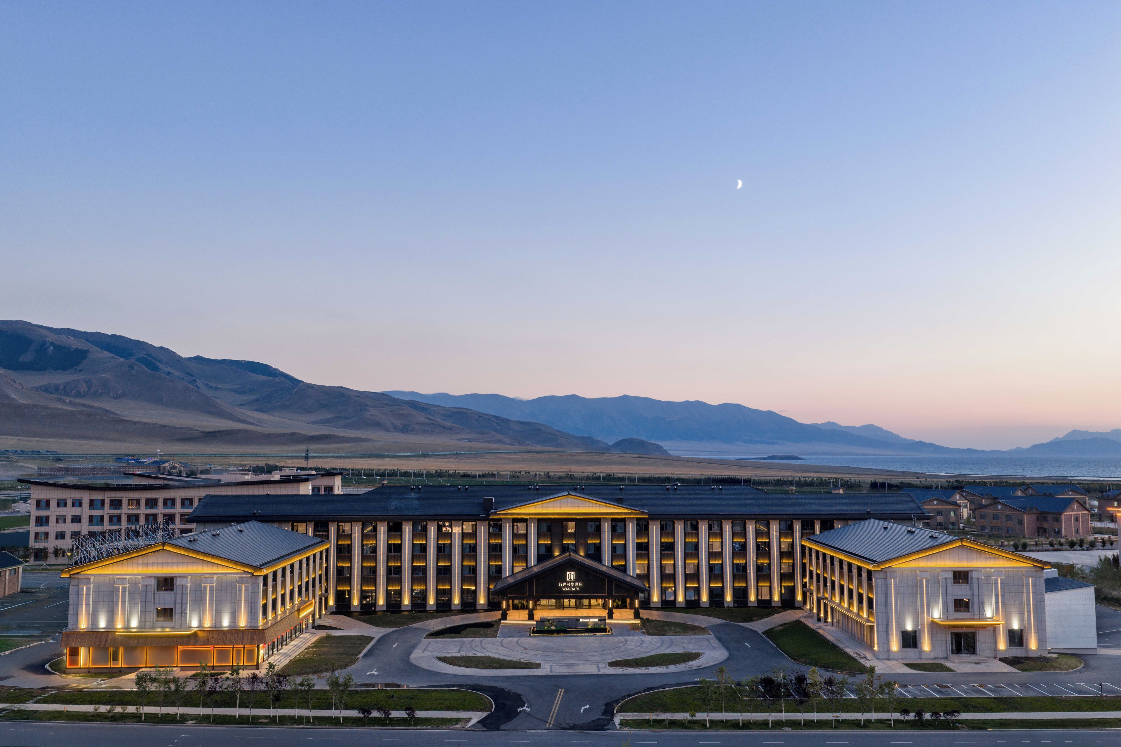 Un hotel moderno con entrada central, varias alas y vistas a montañas al fondo.