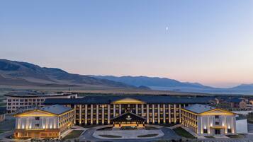 Un hotel moderno con entrada central, varias alas y vistas a montañas al fondo.