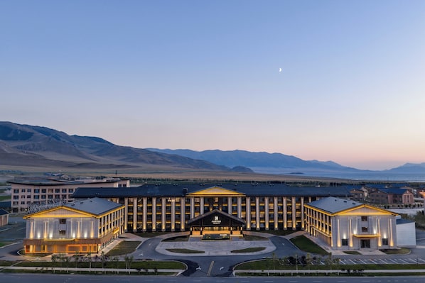 A modern hotel with a central entrance, multiple wings, and a view of mountains in the background. - Wanda Yi Sayram Lake (Bole)