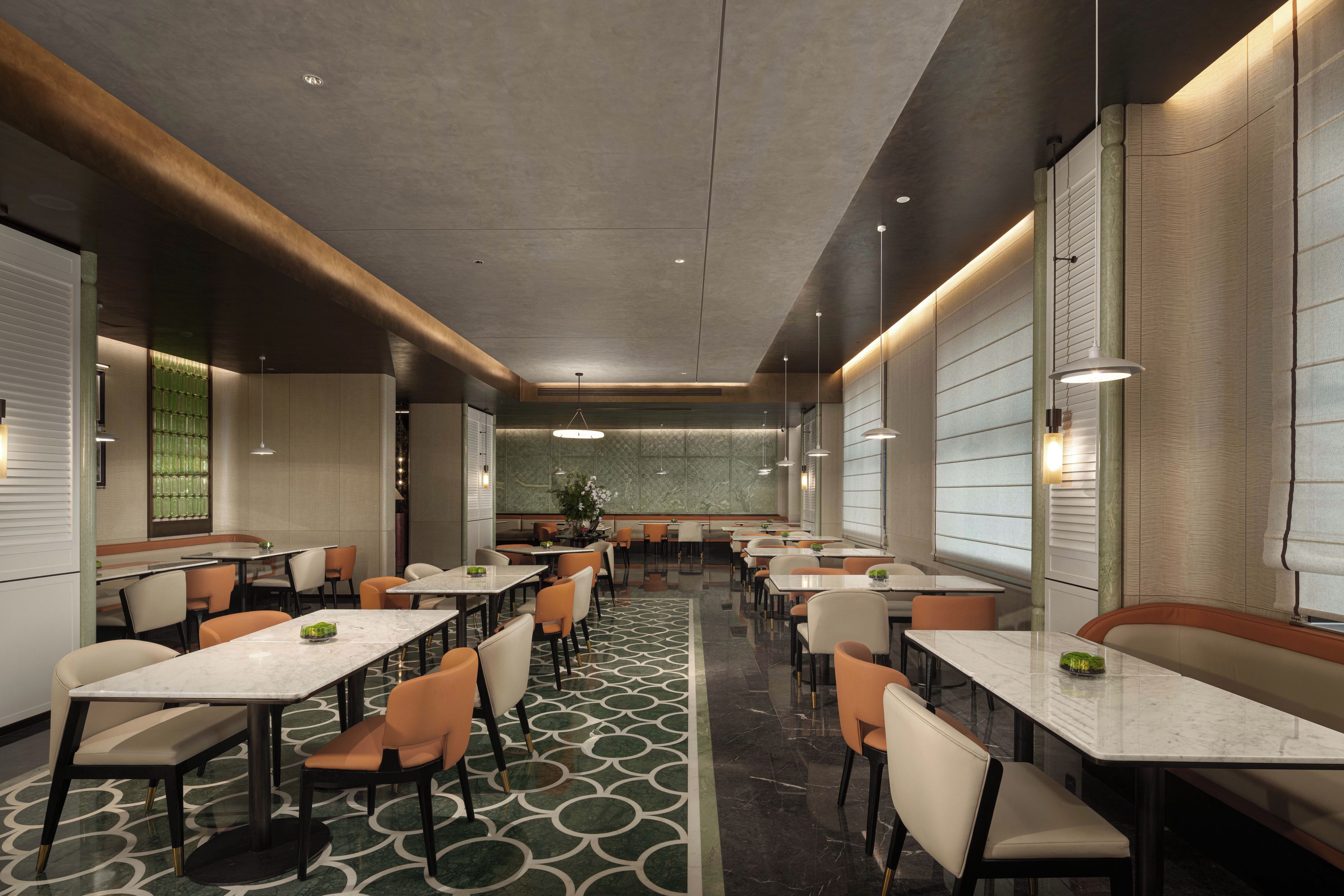 Un interior de restaurante moderno con mesas de mármol, sillas acolchadas e iluminación colgante.