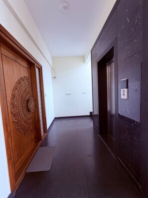 Ein Korridor mit einer Holztür mit aufwendigen Schnitzereien, einer dunklen Wand mit strukturierter Oberfläche und einem hellen Boden.