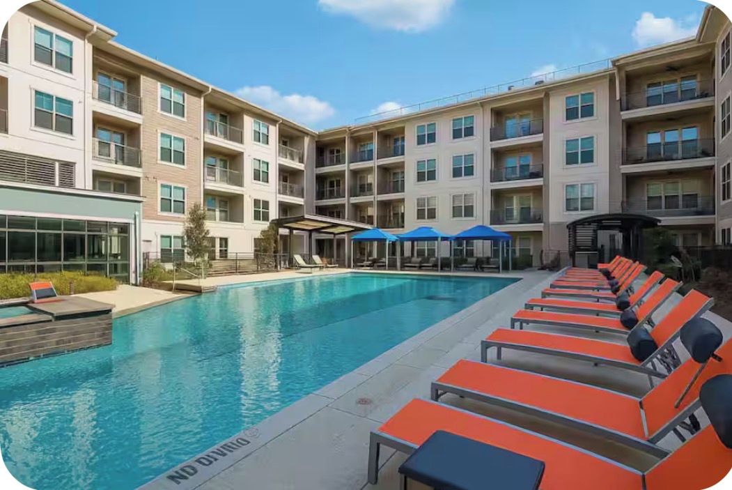 A swimming pool with lounge chairs and a building with multiple balconies.
