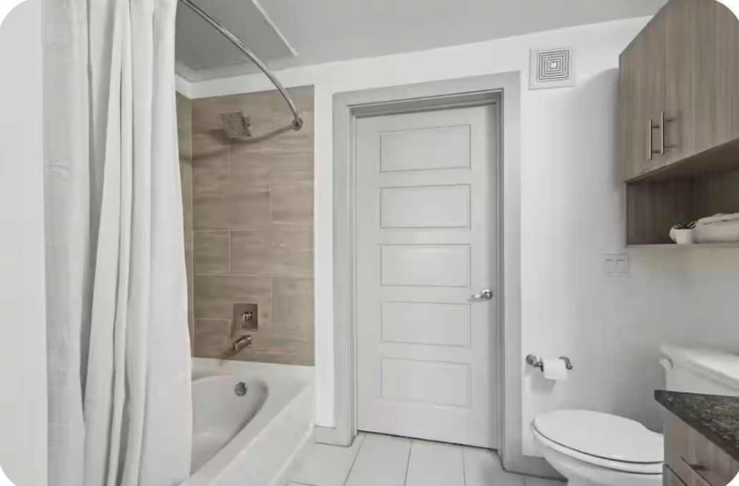 A bathroom with a bathtub, toilet, and wooden cabinets.