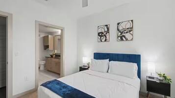 A bedroom with a bed, bedside tables, a nightstand, a mirror, and abstract wall art.