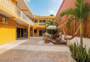 A courtyard with a tiled floor, a hammock, a table with a laptop, and a potted plant. - 6 Guests, 2 Suites, 1 Prime Address: 5th Ave, ADO, Beach, Cozumel Ferry 4 Mins (Playa del Carmen)