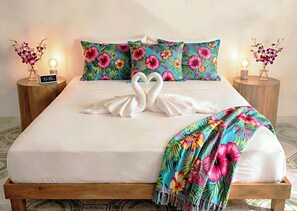 A bed with a white sheet, two pillows with a tropical floral pattern, and a towel arranged in the shape of two swans. There are two bedside tables with lamps and a clock on one. - 6 Guests, 2 Suites, 1 Prime Address: 5th Ave, ADO, Beach, Cozumel Ferry 4 Mins (Playa del Carmen)