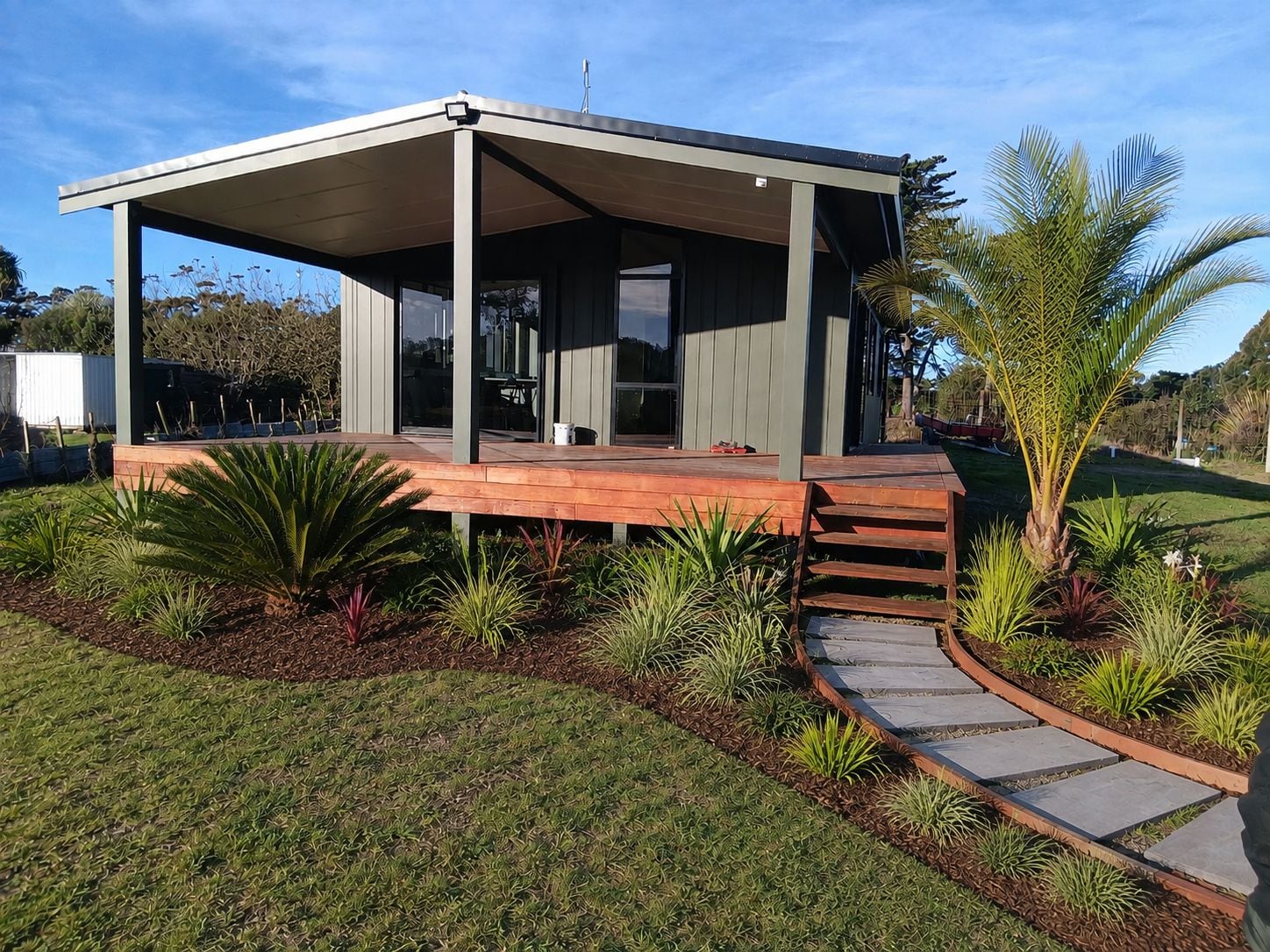 A modern house with a covered patio, a paved walkway, and a variety of plants.