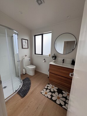 A modern bathroom with a glass shower enclosure, a toilet, a sink with a mirror, and a window.