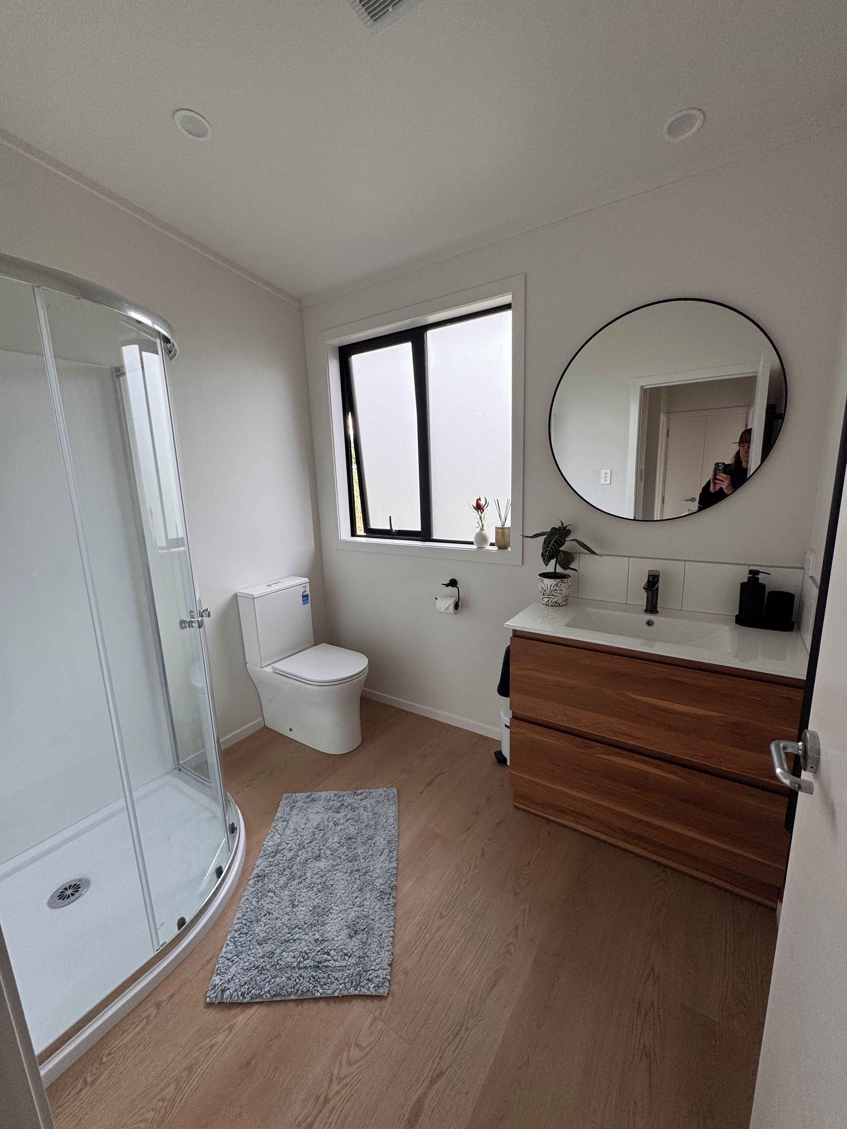 Un baño con cabina de ducha de vidrio, inodoro, lavabo con espejo y ventana.