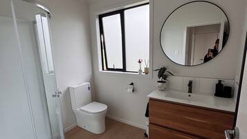 Un baño con cabina de ducha de vidrio, inodoro, lavabo con espejo y ventana.
