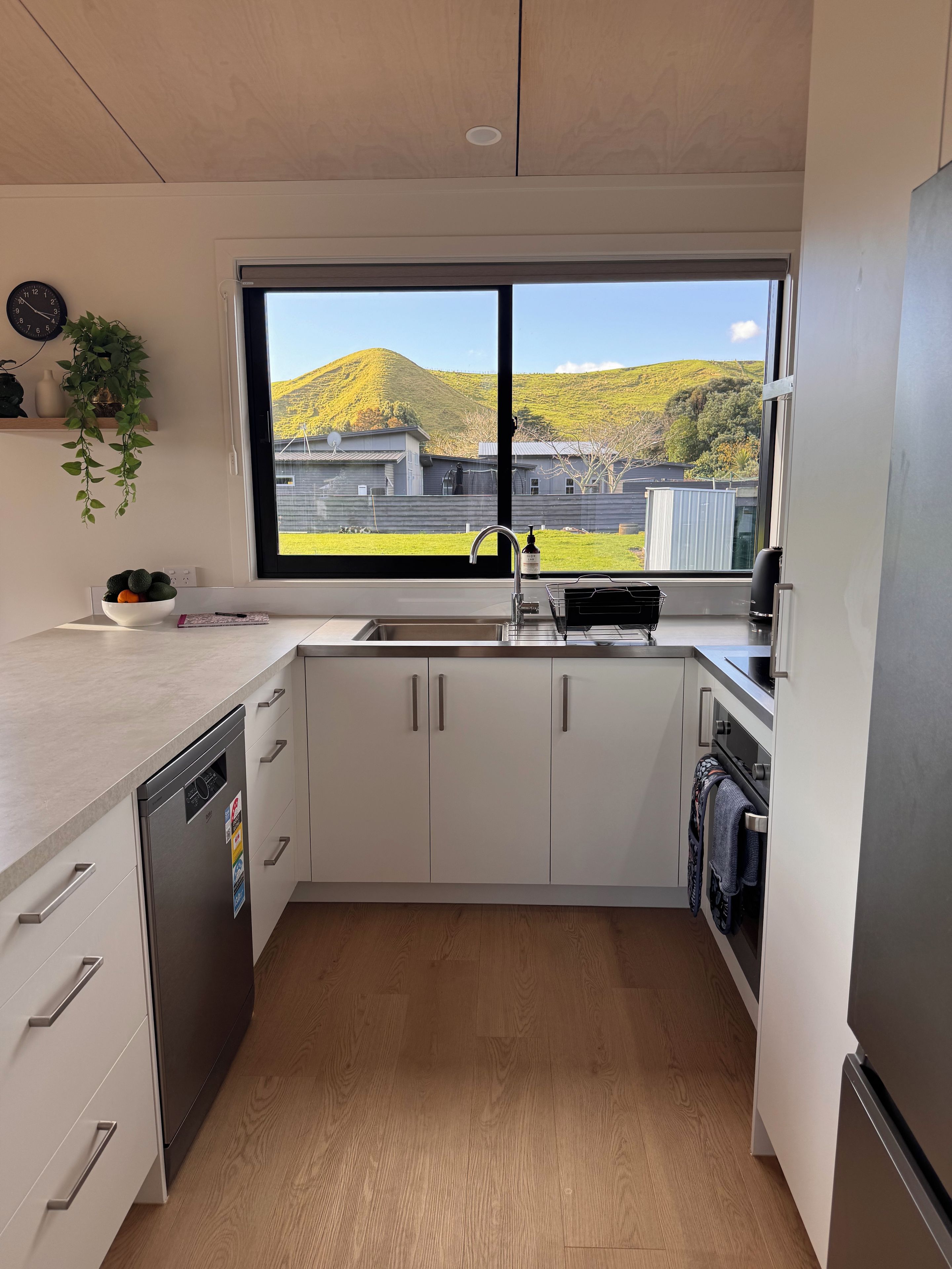 A modern kitchen with a dishwasher, sink, and oven. There is a window with a view of a hilly landscape.