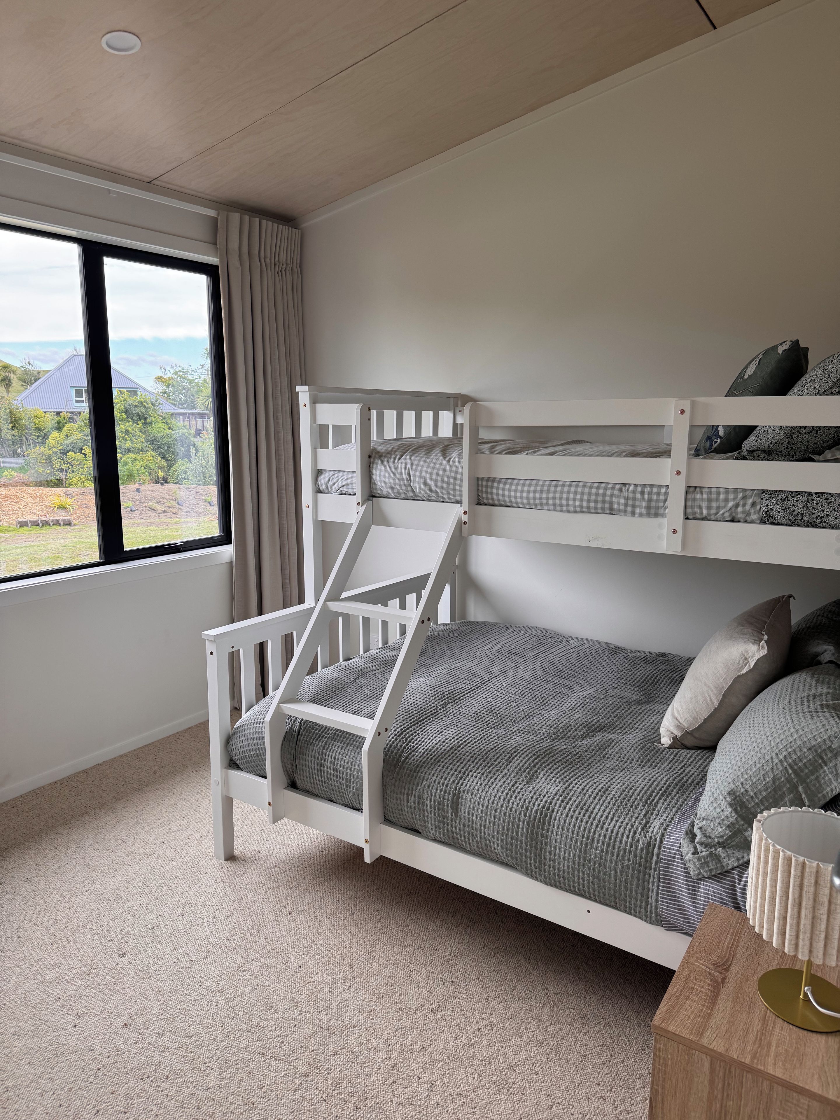 A bunk bed with a view of a house and garden through a window.