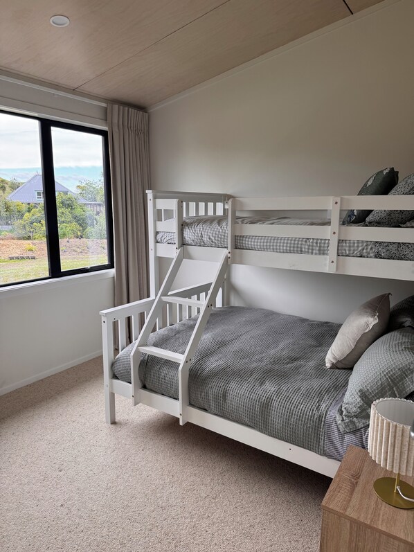 A bunk bed with a view of a house and garden through a window.