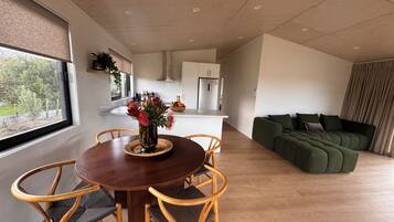A modern living space with a dining area, a green sofa, and a kitchen in the background.