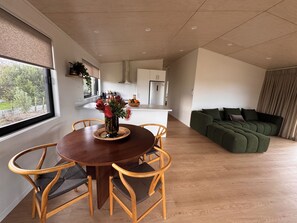 A modern living space with a dining area, a green sofa, and a kitchen in the background. - WAINUI SUNSET HIDEAWAY
WHERE EVERY EVENING ENDS WITH A BEAUTIFUL SUNSET (Gisborne)