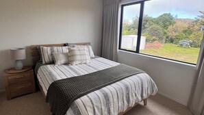 Een slaapkamer met een groot bed, een nachtkastje, een lamp en een raam met uitzicht op groen.