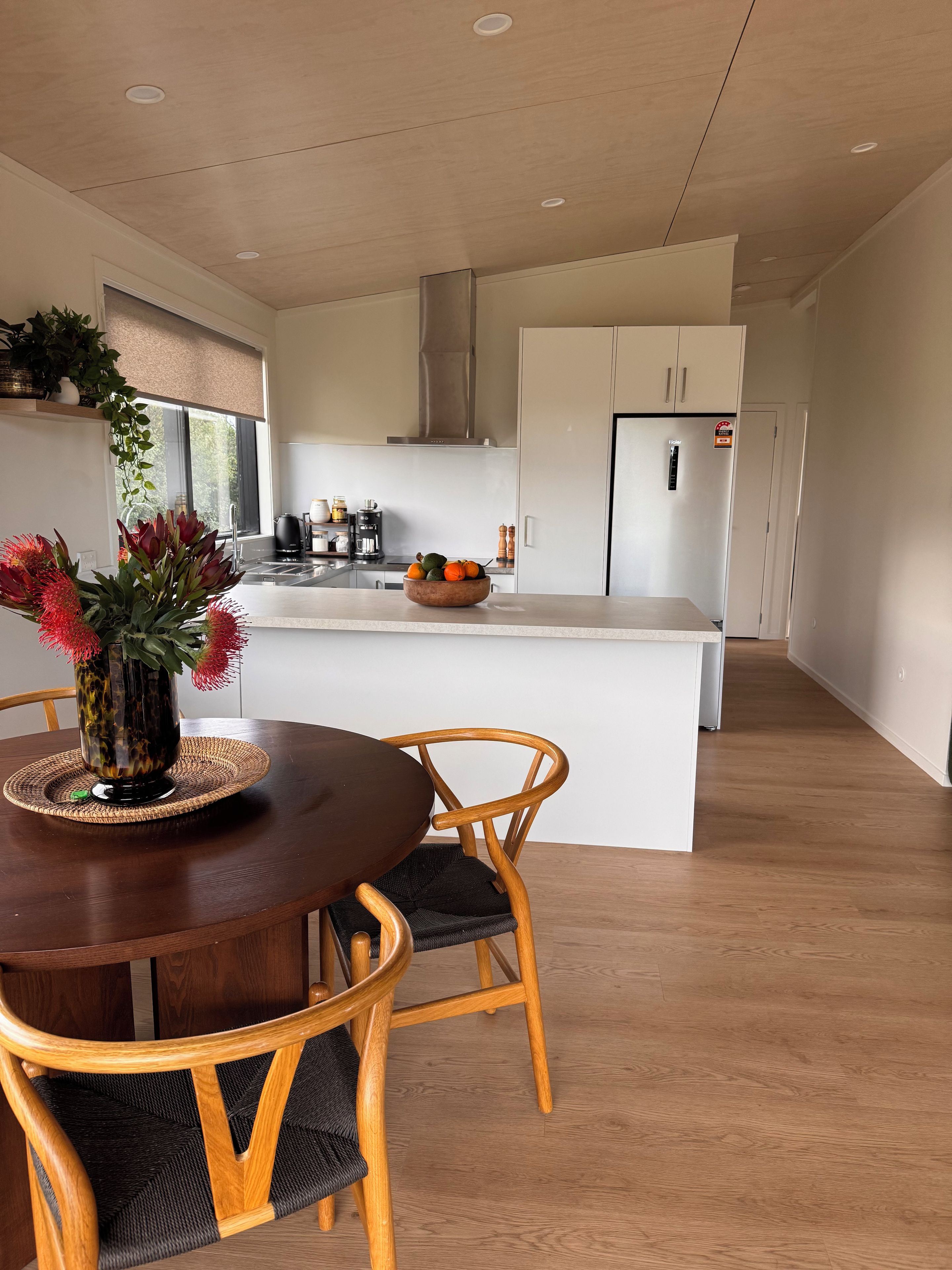 A modern kitchen with a central island, wooden chairs, and a dining table with a vase of flowers.