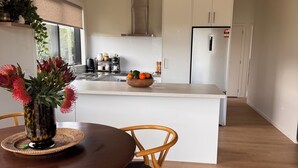 Een moderne keuken met een centraal kookeiland, houten stoelen en een eettafel met een bloemenvaas.