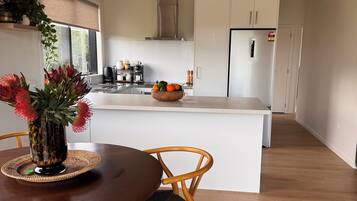 A modern kitchen with a central island, wooden chairs, and a dining table with a vase of flowers.