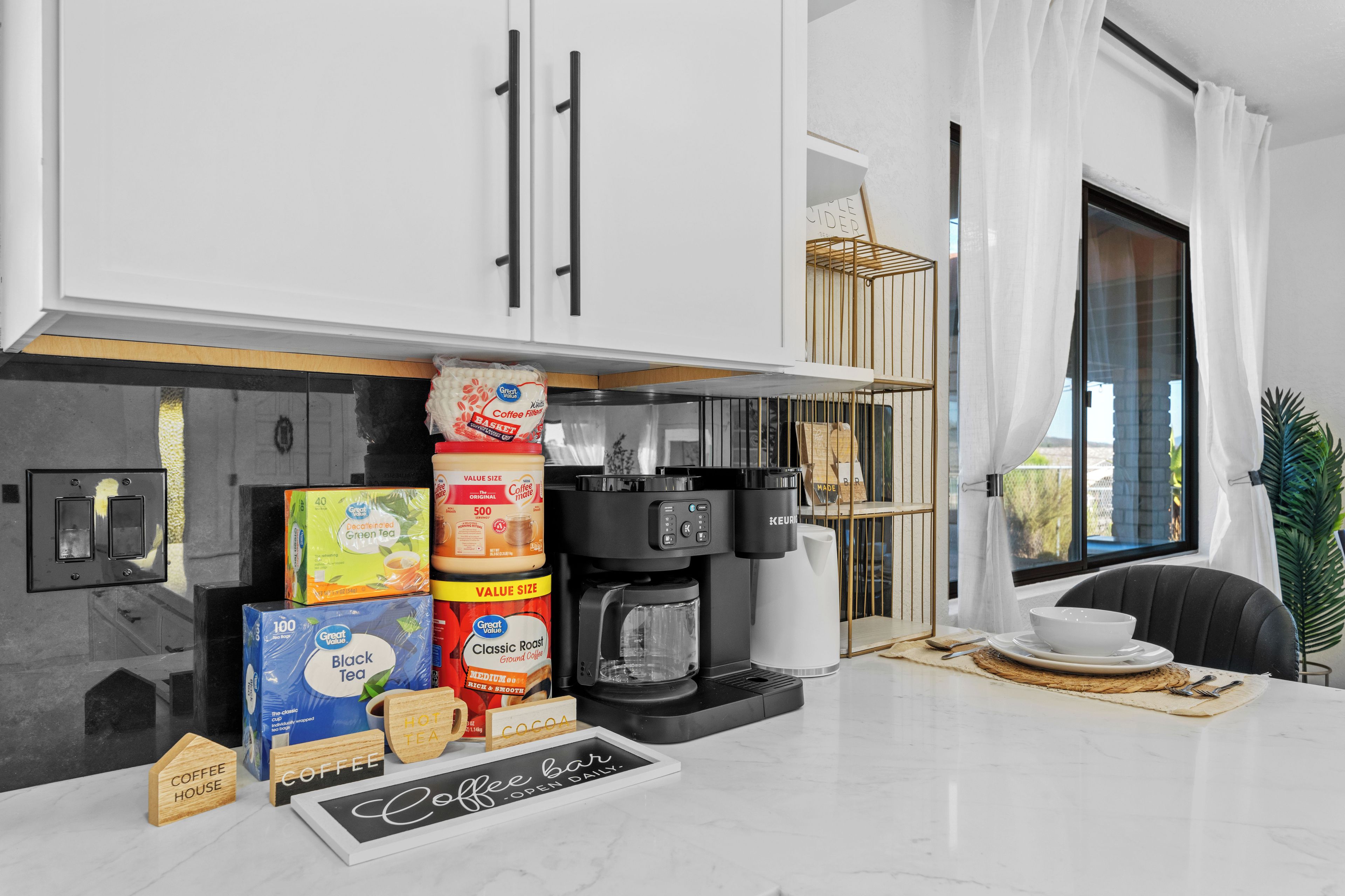 A modern kitchen with white cabinets, a coffee maker, and various coffee and tea products.