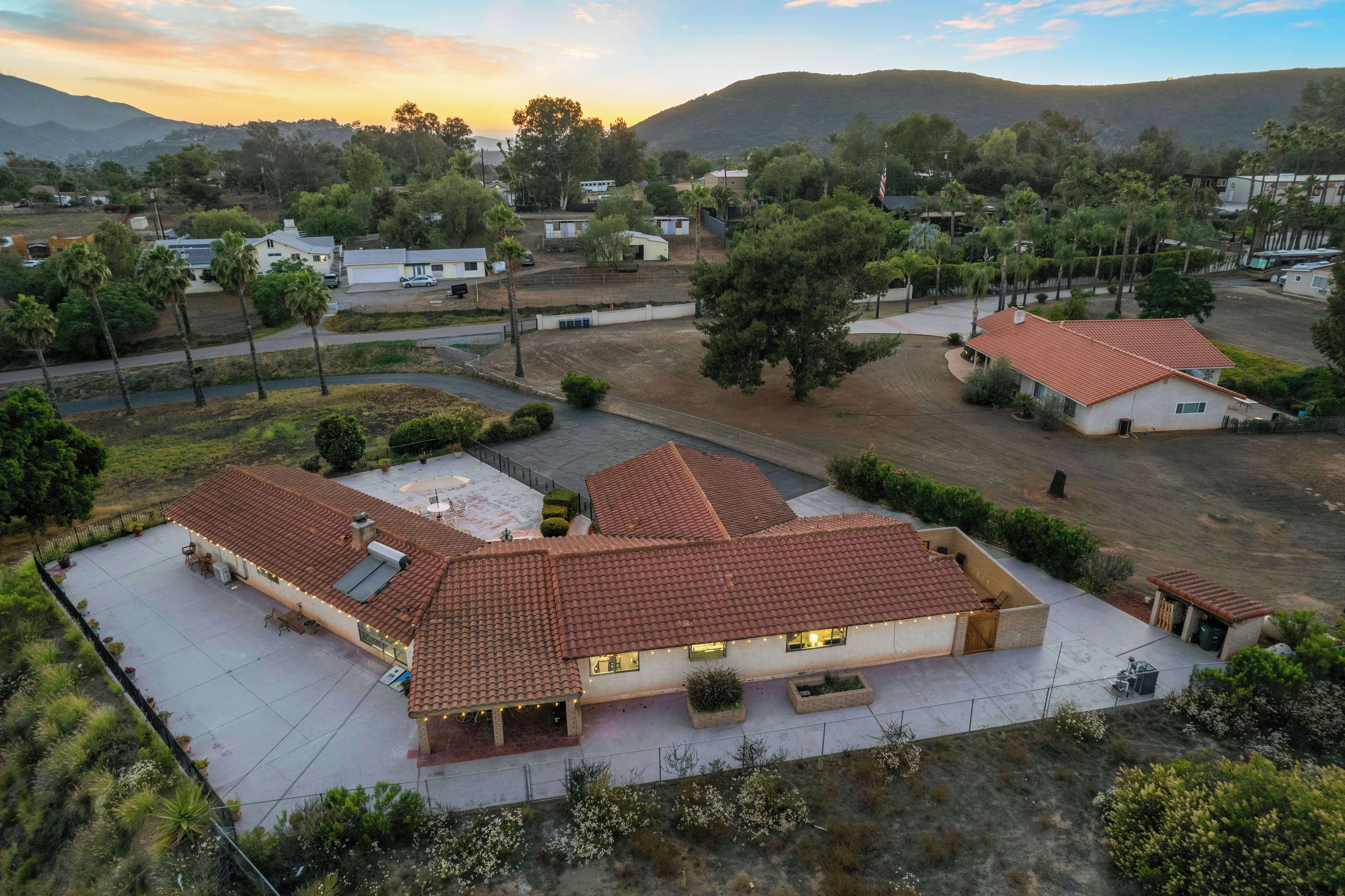 Zona residencial com casas com telhados vermelhos, cercada por vegetação e colinas ao fundo.