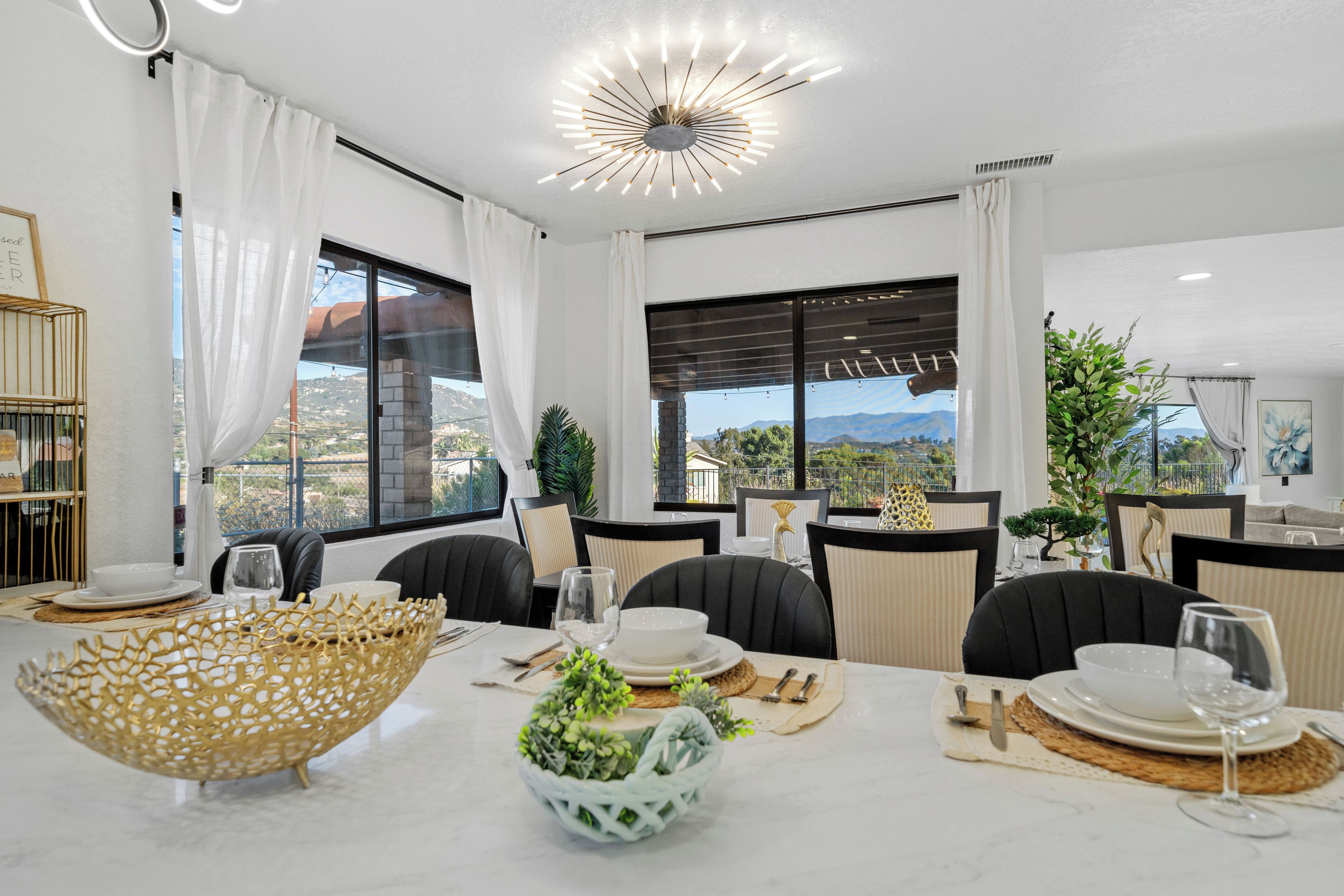 A modern dining area with a large table set for four, featuring a decorative bowl, plates, and glassware.