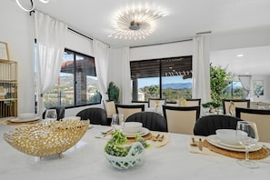 A modern dining area with a large table set for four, featuring a decorative bowl, plates, and glassware.