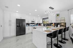A modern kitchen with white cabinetry, a central island with bar stools, and a large refrigerator.