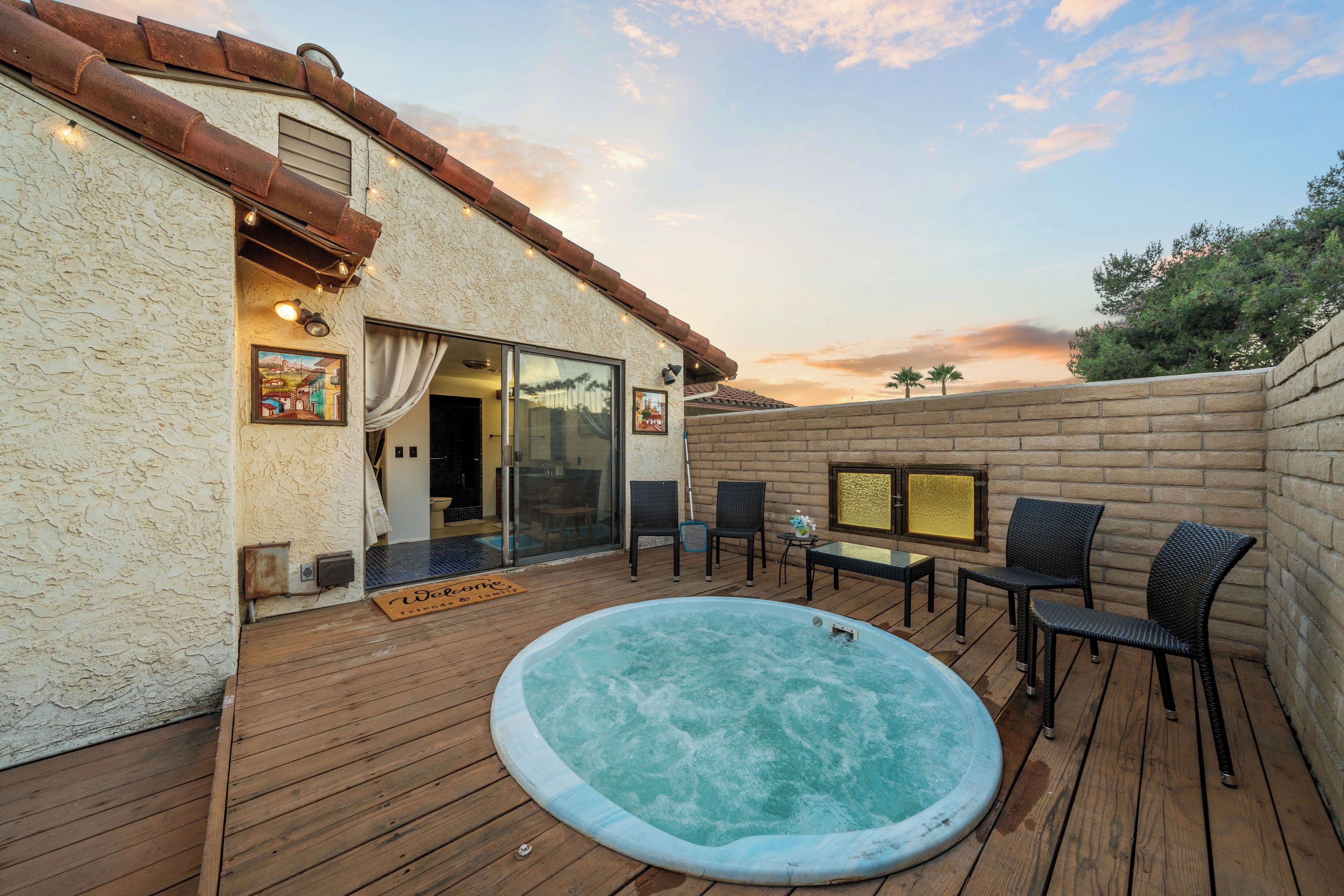 En træterrasse med jacuzzi, udendørs møbler og en fransk dør, der fører ind til et rum.