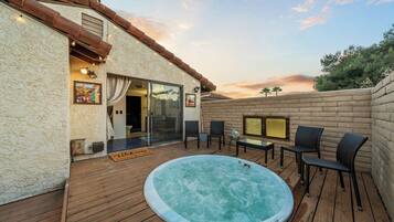 En træterrasse med jacuzzi, udendørs møbler og en fransk dør, der fører ind til et rum.