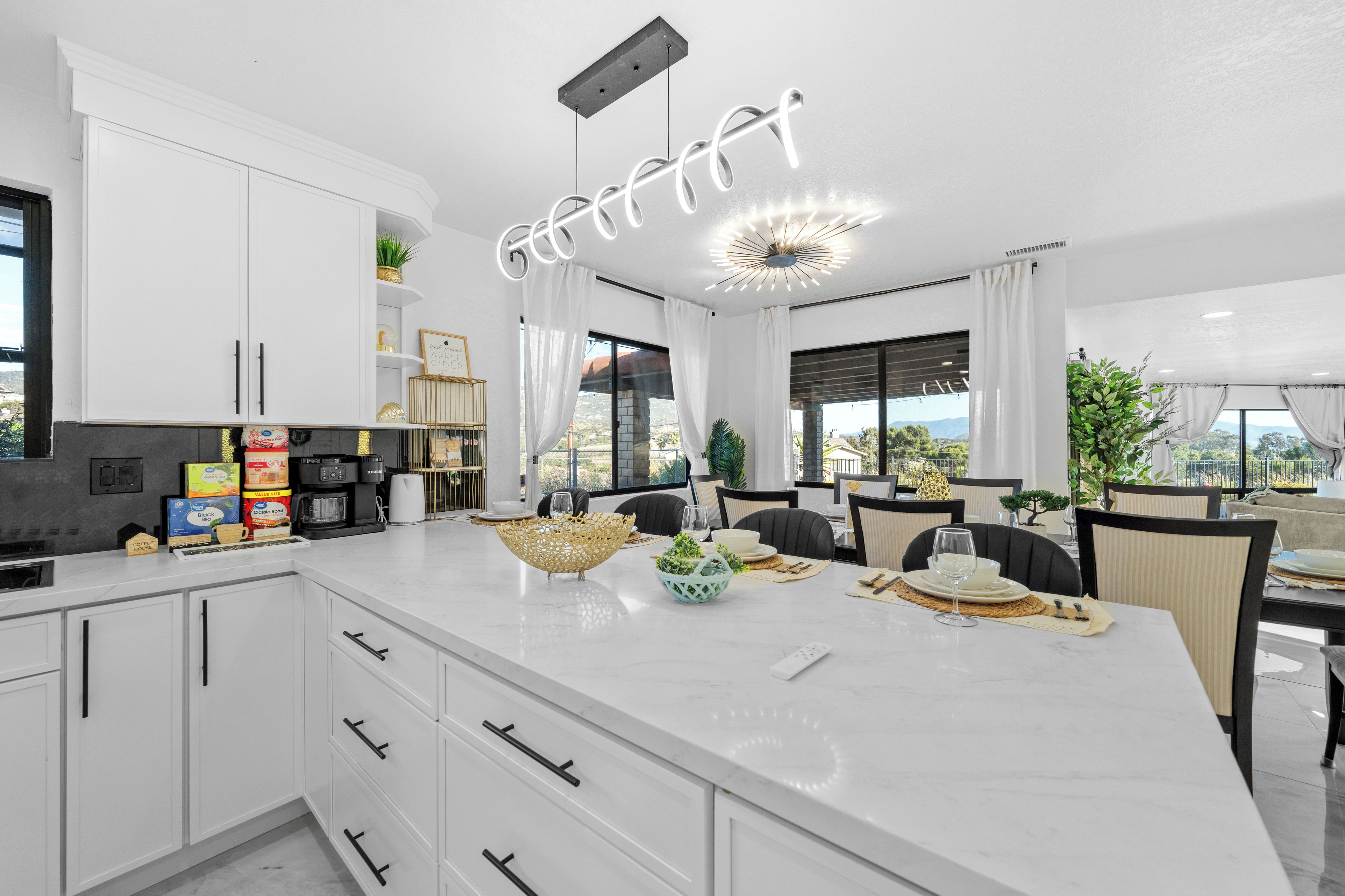 A modern kitchen with white cabinets, a marble countertop, and a dining area with a table set for two.