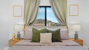 Ein Schlafzimmer mit einem Bett, grünen und beigen Kissen, Blick auf eine Landschaft durch ein Fenster und zwei Nachttische mit Lampen.