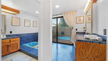 A bathroom with a blue-tiled bathtub, wooden vanity, and a large mirror with lights.