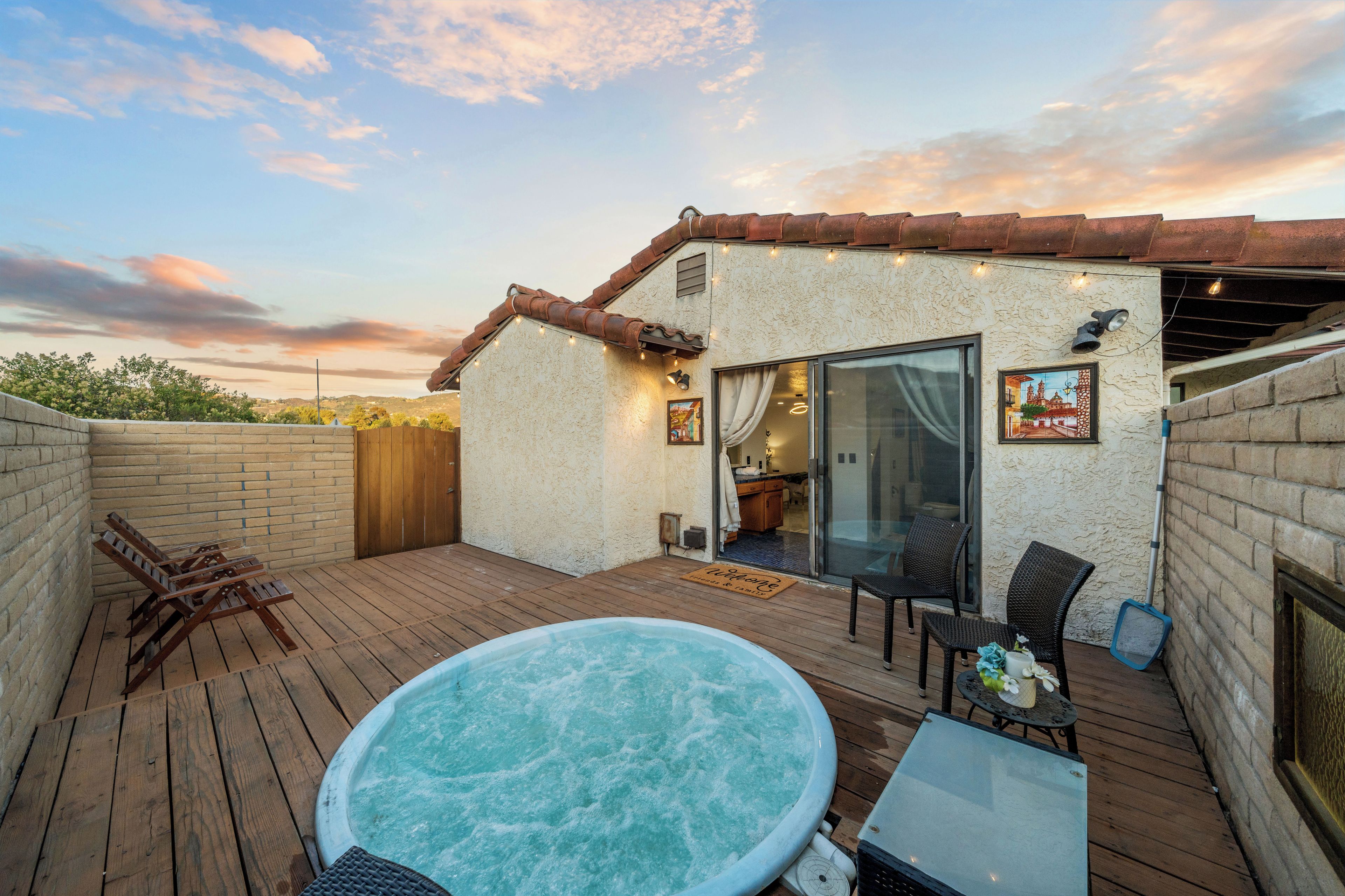 A wooden deck with a hot tub, outdoor seating, and a brick wall.