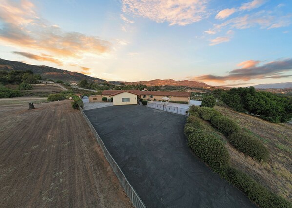 A large, open parking area with a paved driveway leading to a building with a red-tiled roof.