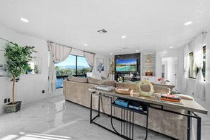 A modern living room with a large window, a sofa, a coffee table, and a television. - Mountain View, 2500 sqft, King Bed, Garage, 3BR/2Bth (Jamul)