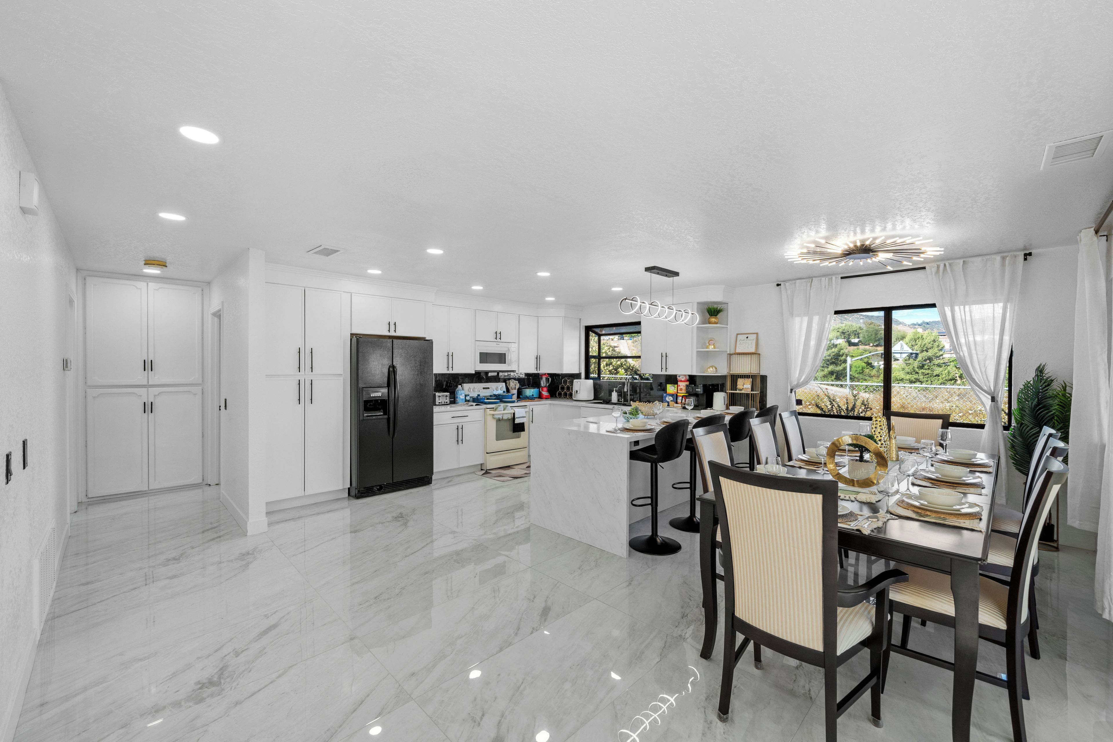 A modern kitchen with white cabinetry, a central island, and a dining area with bar stools.