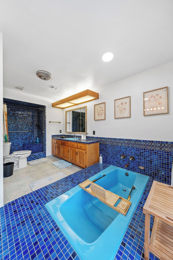 A bathroom with a blue-tiled shower, a bathtub, wooden cabinets, and a sink.