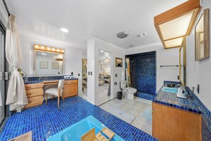 Une salle de bain avec un sol carrelé de carreaux bleus, un meuble-lavabo en bois, un lavabo et un miroir avec éclairage.