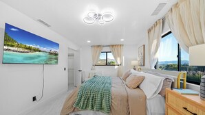 Ein Schlafzimmer mit einem Bett, einem Fenster mit Vorhängen, einem Nachttisch und einem an der Wand montierten Fernseher.