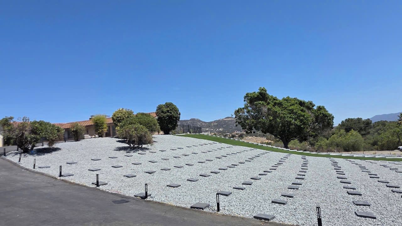 Ein Friedhof mit in Reihen angeordneten Grabsteinen, umgeben von Bäumen und blauem Himmel.