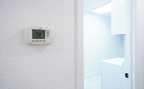 Een thermostaat bevestigd aan een ruwe witte muur, waarop een temperatuur van 23 graden Celsius staat.