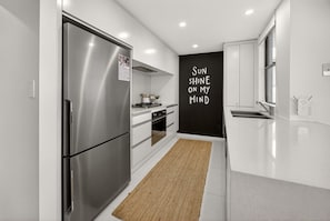 A modern kitchen with stainless steel appliances, a black accent wall with motivational text, and a minimalist design. - Soul@Sunshine - Private Pool, Ocean View (Sunshine Beach)
