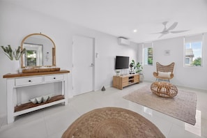 A modern living room with a white console table, a television, a wicker chair, and a large window. - Soul@Sunshine - Private Pool, Ocean View (Sunshine Beach)